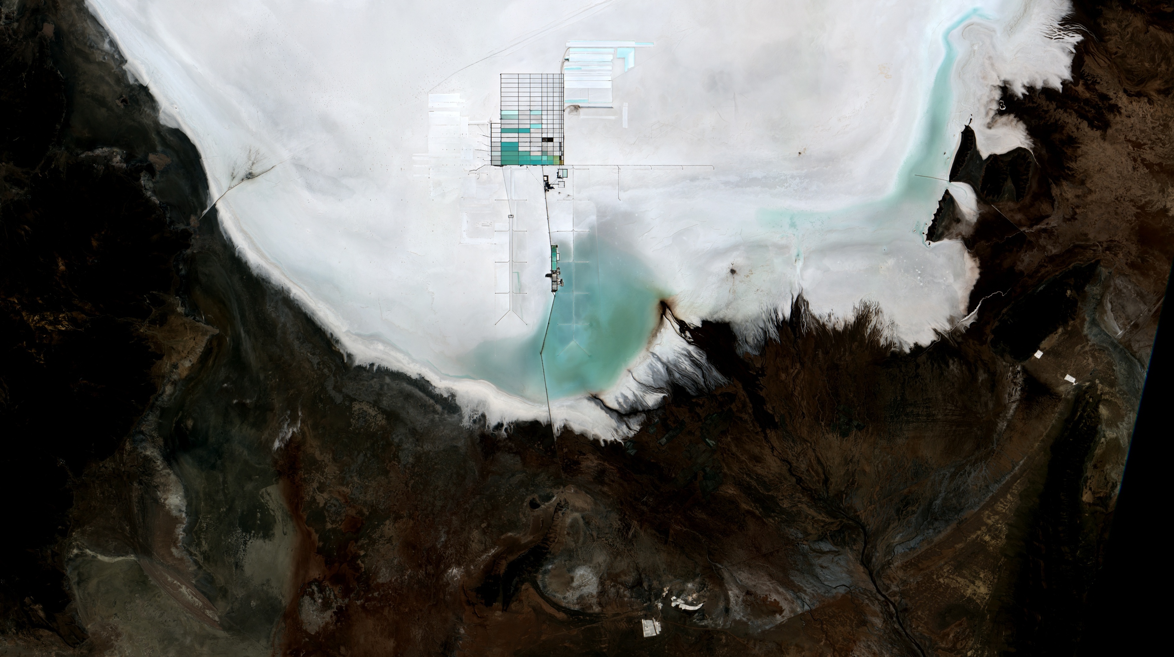 Overhead view of a salt falt with a small section covered with rows of rectangluar evaporation ponds.