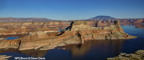 A distinctive, steep rock formation surrounded by smooth water on a clearday. Other rock formations are visible in thedistance.