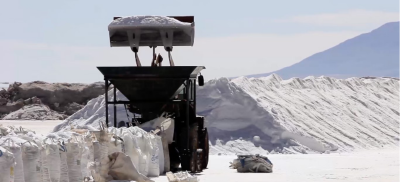 A dumptruck with a basket full of white mineral, which is surrounded by mounds of white mineral